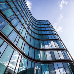 A high rise building in a glass facade with the reflection of the surrounding buildings